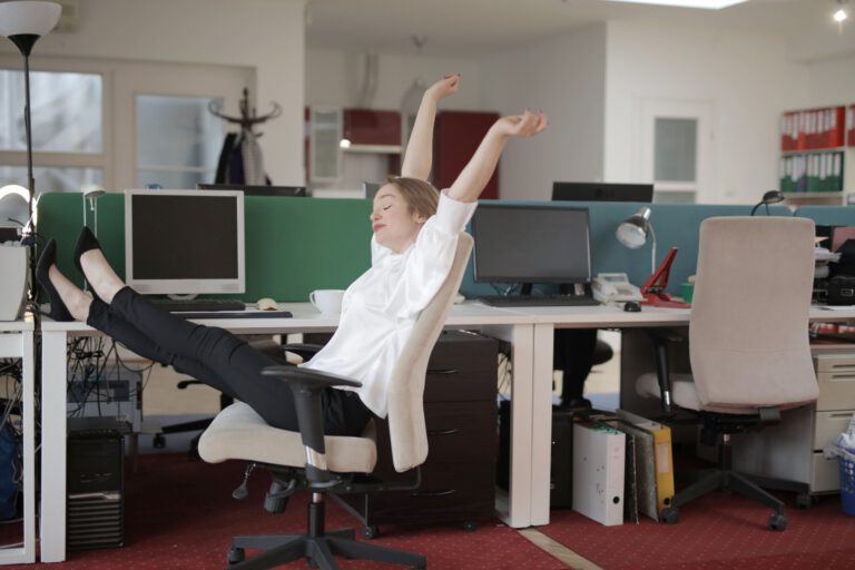 Haltungsanalyse am Arbeitsplatz: Mitarbeiterin unterbricht langes Sitzen mit einer Dehnung am Schreibtisch